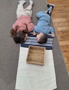 Two Casa students lying on the floor on the Montessori "peace mat" taking a quiet moment together.