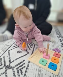 Infant student lying on their stomach plays with a wooden puzzle.