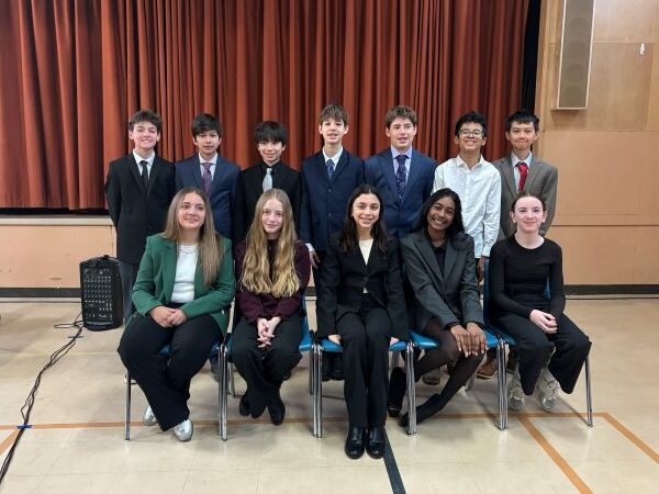 Junior High students sitting and standing in a group in the gymnasium.