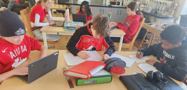 A group of Junior High students wearing Team Canada Jerseys work at their desks together.