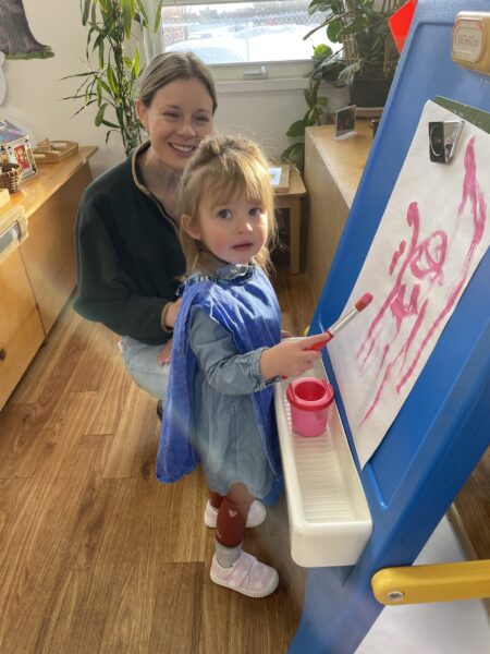 Mom crouches while watching her daughter paint during an open class at schoo;.