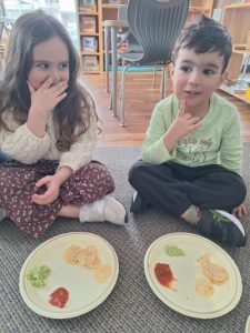 Two Children sit on the floor in front of plates that have guacamole, salsa and tortilla chips.
