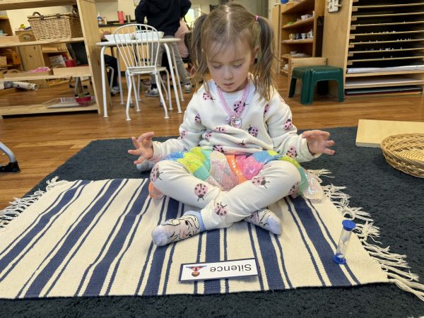 A girl sits on a striped mat with crossed legs, meditating during the Montessori Silence Game.